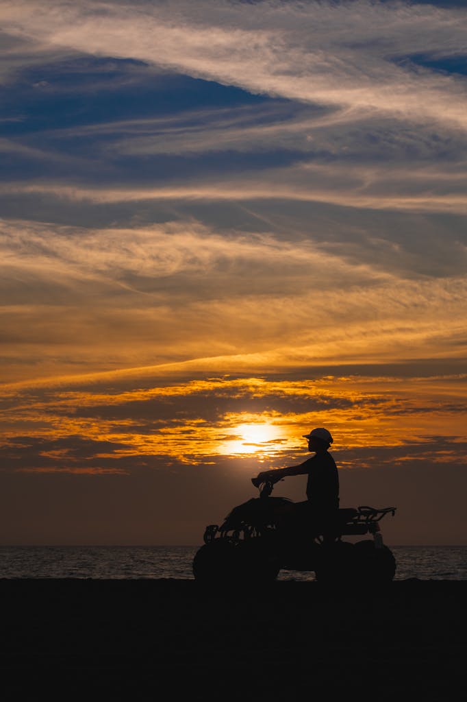 A man rides an ATV along the beach in Paoay, Philippines, silhouetted against a vibrant sunset.