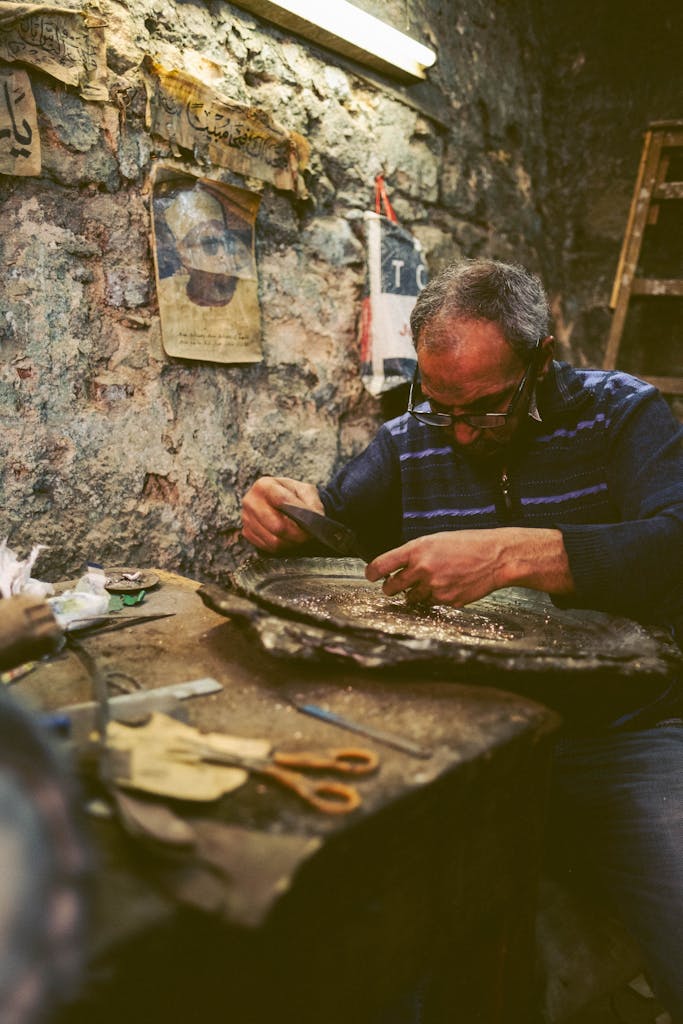 A senior man in an Egyptian workshop focusing on intricate metalwork, surrounded by tools.