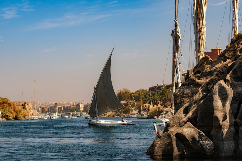 A traditional sailboat glides on the scenic Nile River near Aswan, Egypt, showcasing a tranquil landscape.