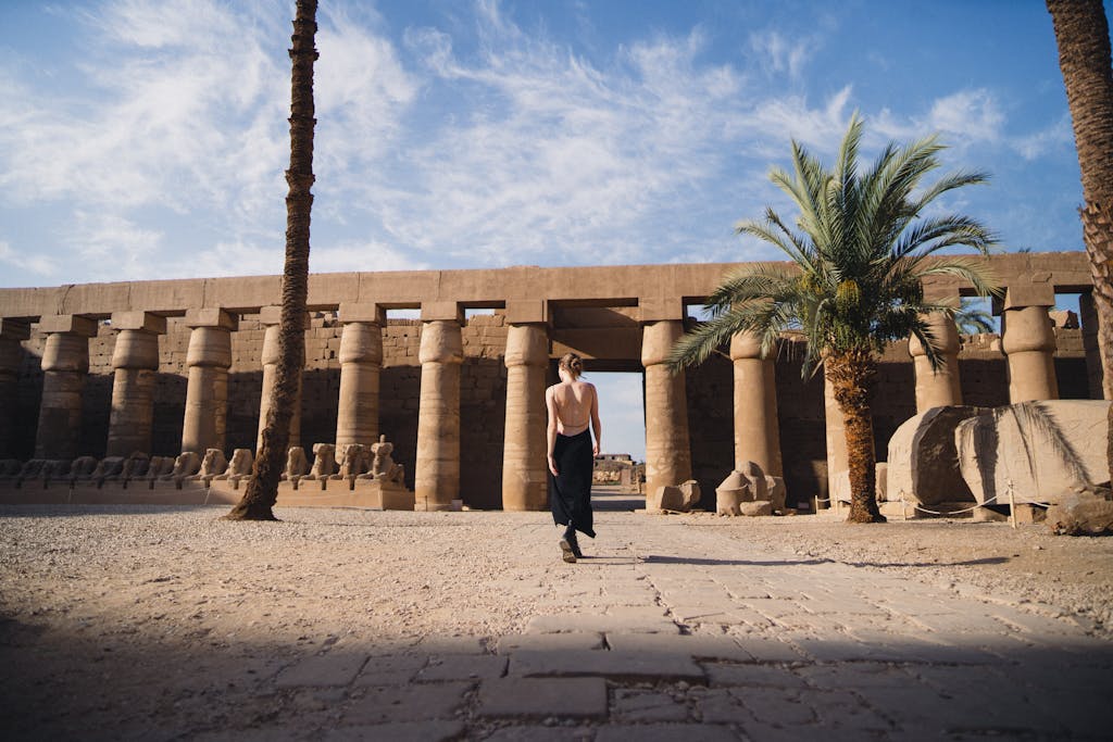 A woman in a backless black dress walking at the historic Karnak Temple in Egypt.