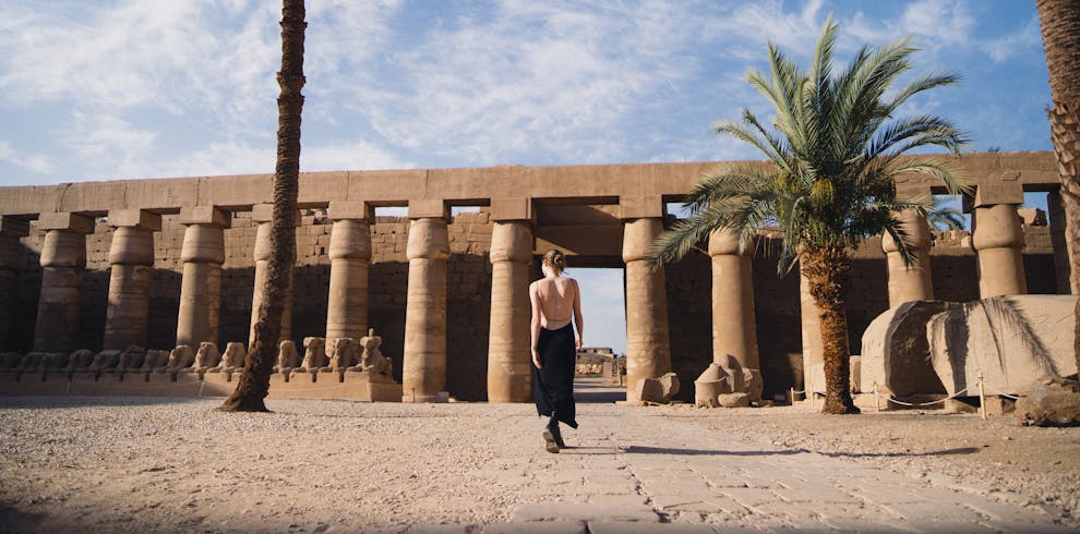 A woman in a backless black dress walking at the historic Karnak Temple in Egypt.