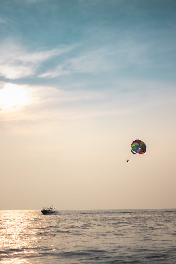 Colorful parasailing experience over a calm ocean at sunset with a boat in view.