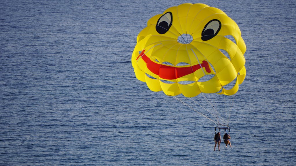 Couple enjoying parasailing with a smiley parachute over the ocean on a sunny day.