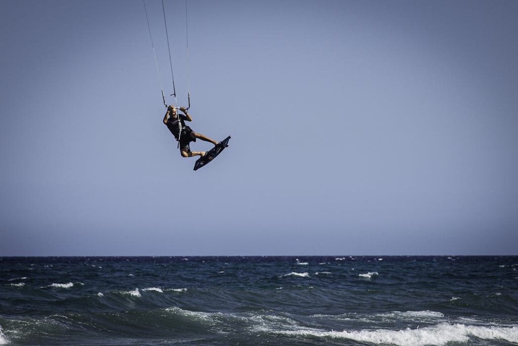 Exciting kiteboarding scene as a man soars over the ocean waves under a clear sky.