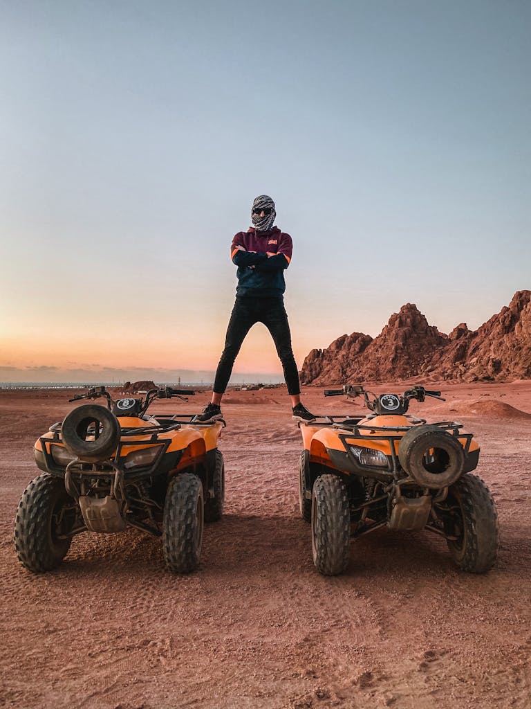 Man on quads with arms crossed, exploring Sinai's desert at sunset.