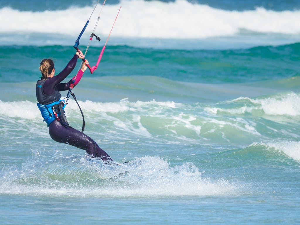 Woman engaging in thrilling kiteboarding on ocean waves during daytime.